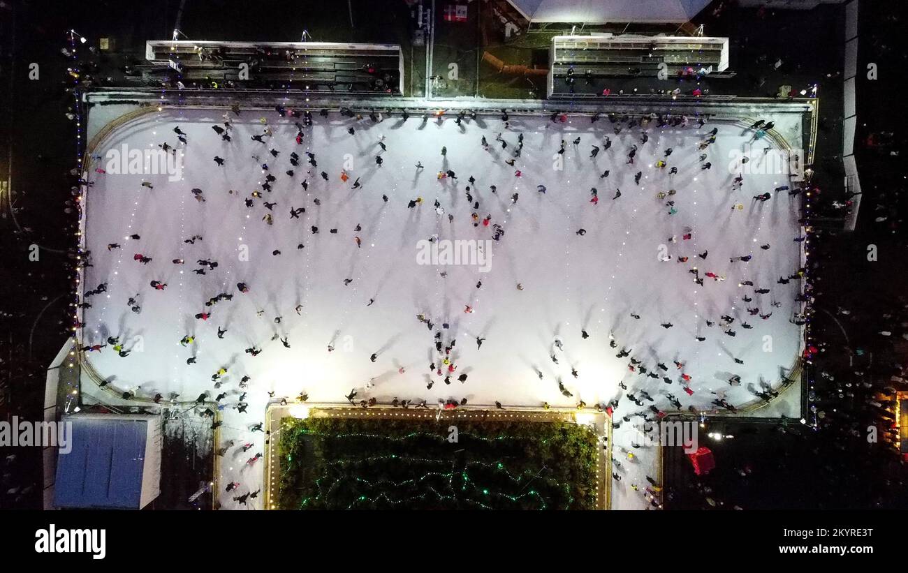 Drone View Flug über viele Menschen, die im Winter auf einer Freiluft-Eislaufbahn Schlittschuhlaufen. Eislaufen, Draufsicht. Eisbahn Im Stadtpark. Outdoor-Aktivitäten. Weihnachtsbeleuchtung am Neujahrstag. Feiertage Stockfoto