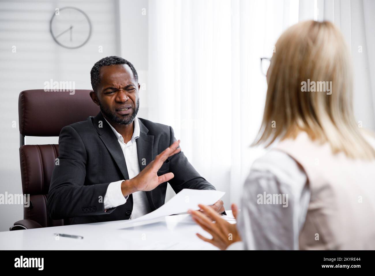 Einstellung, Vorstellungsgespräch. Ein afroamerikanischer Geschäftsführer mittleren Alters, der ein Vorstellungsgespräch in einem hellen Büro abhält. Er sieht sich den Lebenslauf an, er mag ihn nicht Stockfoto