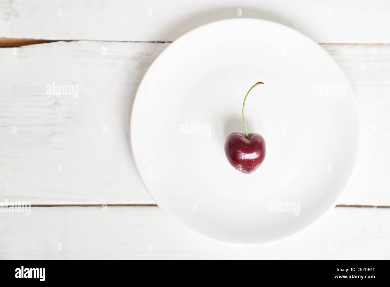 Eine herzförmige Kirsche auf einem weißen Teller. Reife, frische, saftige Beere auf weißem Hintergrund. Fruchthintergrund. valentinstag. Mit Platz zum Kopieren. Hochwertiges Foto Stockfoto