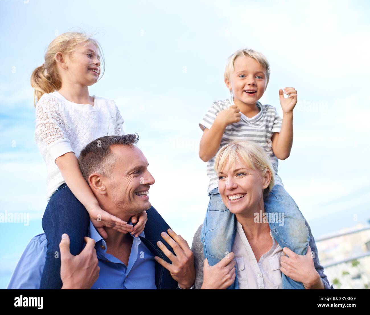 Ich verbringe schöne Zeit mit Mami und Daddy. Bildausschnitt von zwei Eltern, die ihre Kinder auf den Schultern im Freien tragen. Stockfoto