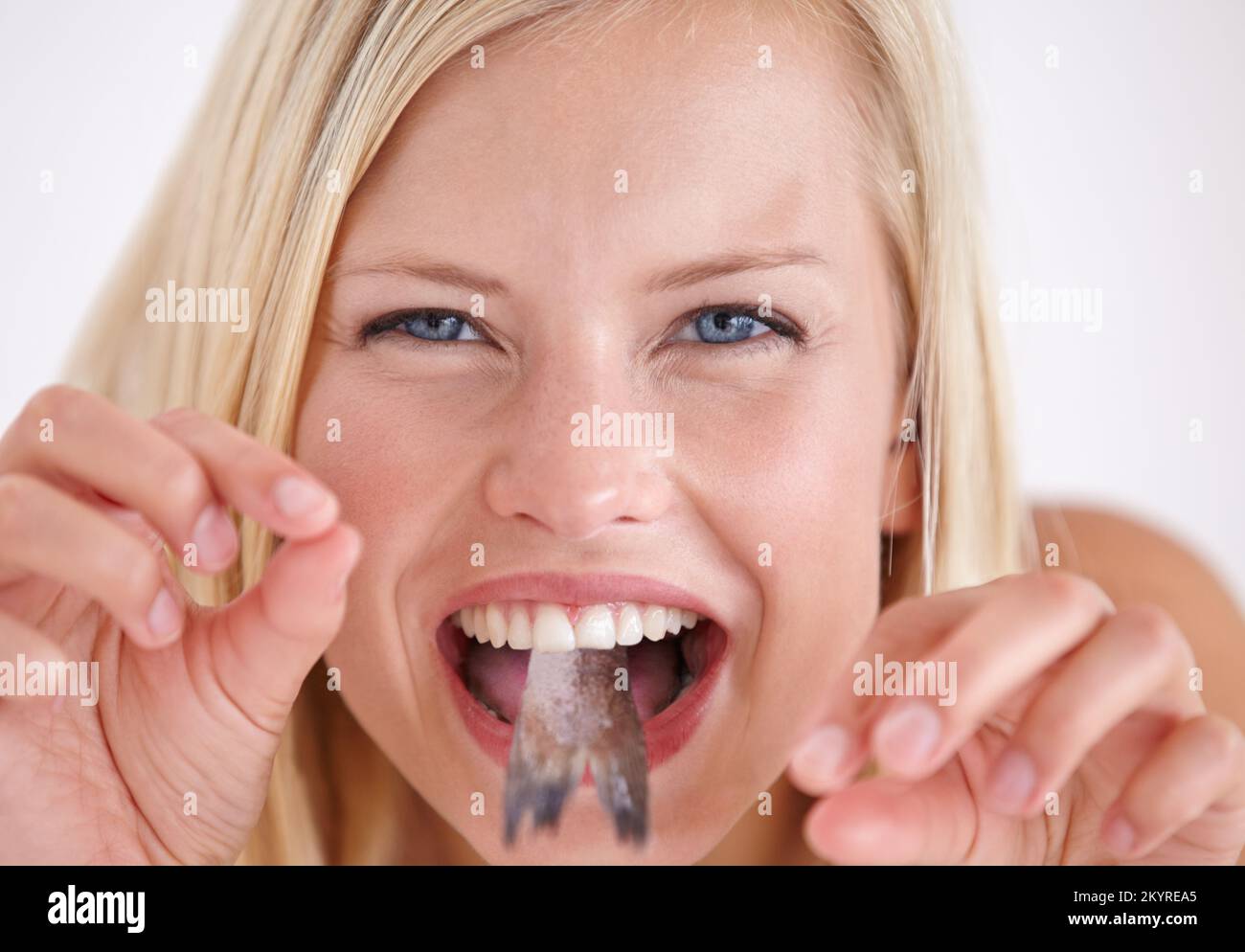 Ich kann nicht glauben, dass ich das esse. Eine junge Frau, die ein Gesicht mit einem Fisch im Mund zieht. Stockfoto