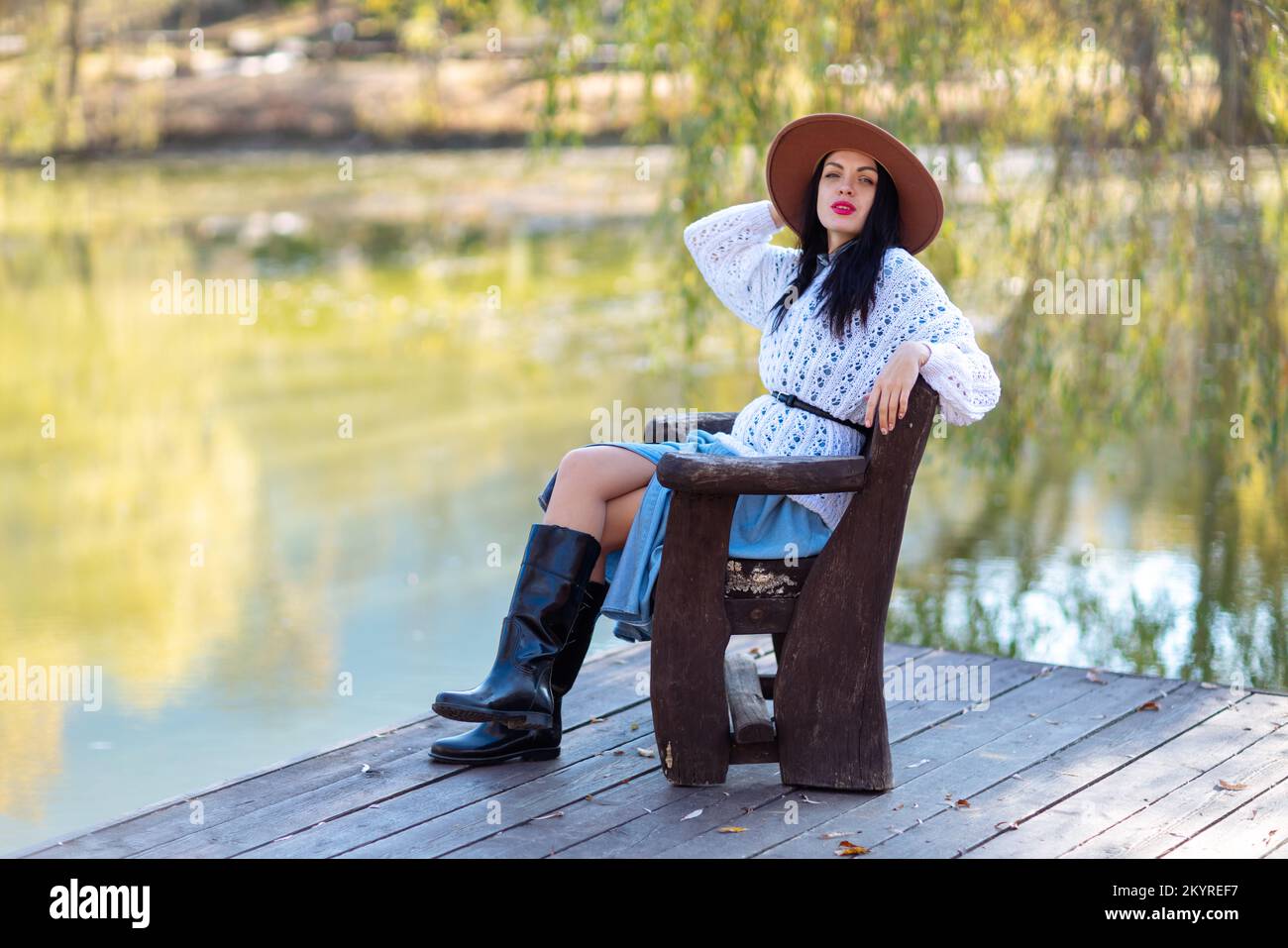 Herbstsee-Frau. Sie sitzt im Herbst an einem Teich auf einem hölzernen Pier und bewundert die Natur. Das Konzept des Tourismus, Wochenenden außerhalb der Stadt. Stockfoto