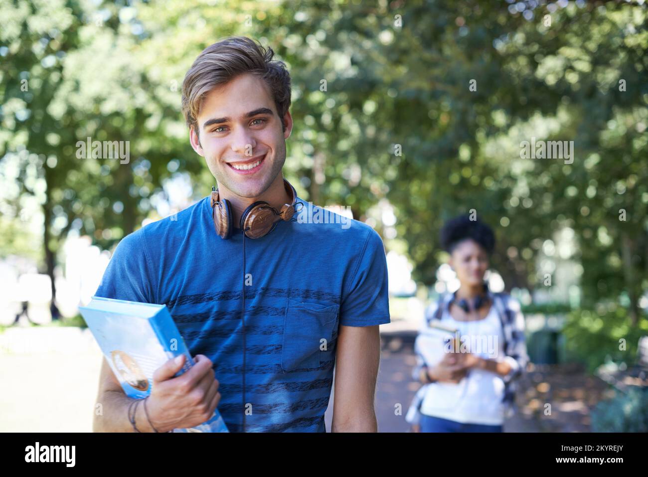 Ich liebe das College-Leben. Porträt eines gutaussehenden Schülers, der mit seinem Lernmaterial in einem Park spaziert. Stockfoto