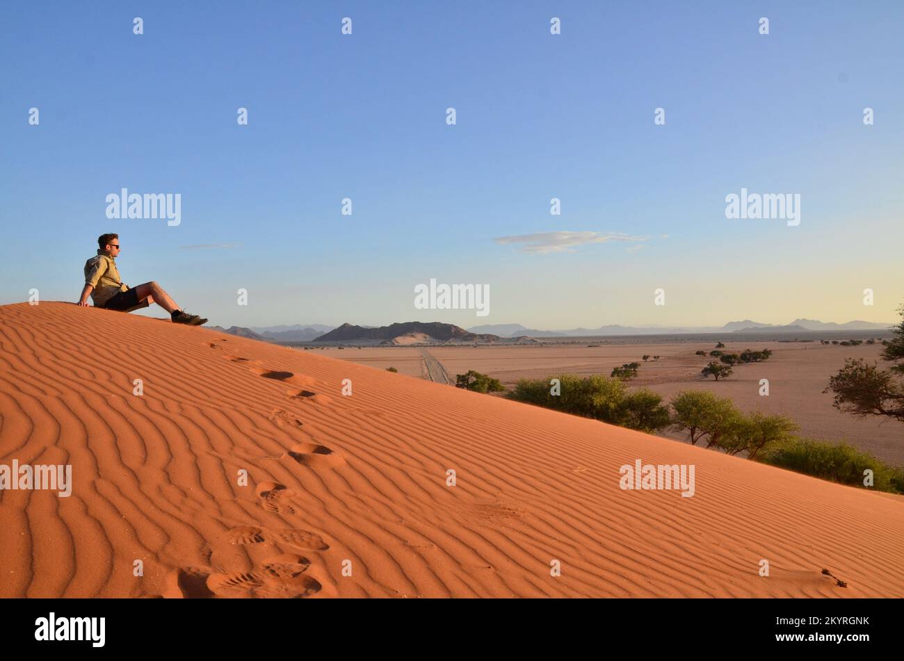 Mann sitzt auf der Düne in der Trockenpfanne des Sossusvlei Namib Naukluft Nationalparks Stockfoto