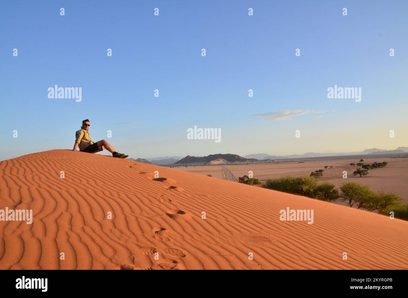 Mann sitzt auf der Düne in der Trockenpfanne des Sossusvlei Namib Naukluft Nationalparks Stockfoto