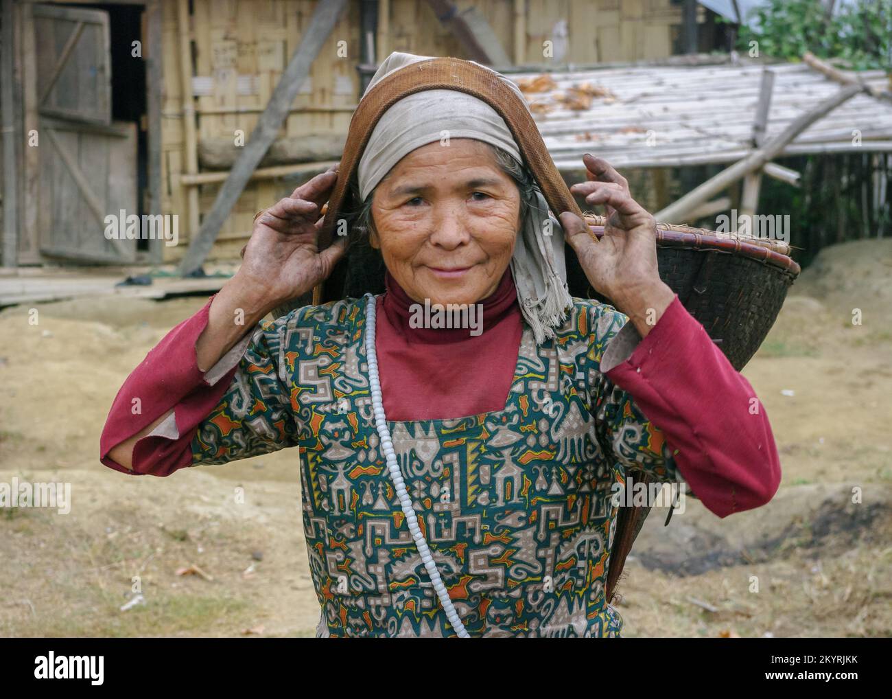 Raga, Arunachal Pradesh, Indien - 11 14 2010 : ländliches Außenporträt einer lächelnden alten Nyishi-Stammesfrau, die einen konischen, gewebten Korb mit Kopfband trägt Stockfoto