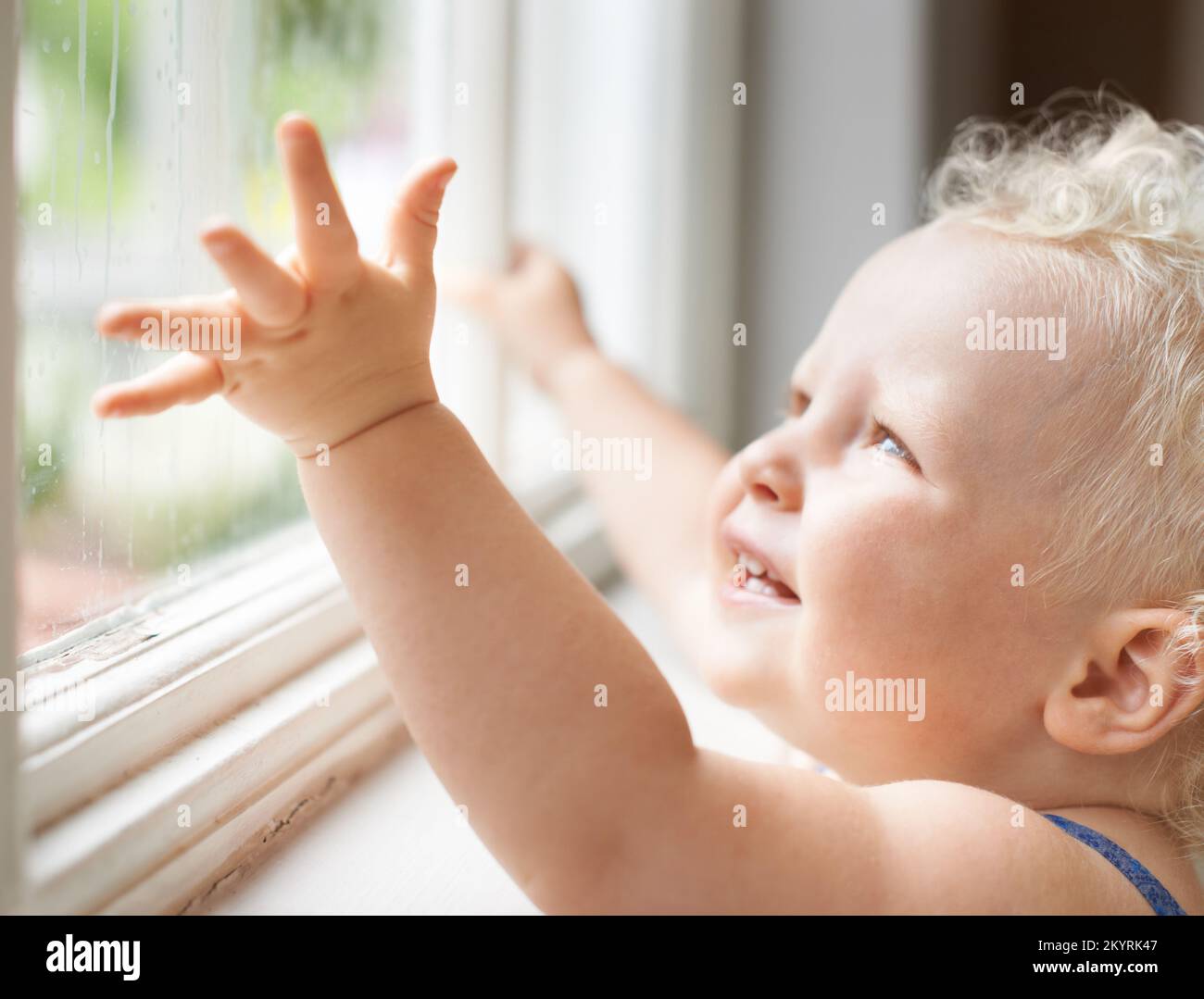 Sie starren in Staunen über die Welt. Ein süßes kleines Kleinkind, das aus Verwunderung durch ein Fenster schaut. Stockfoto