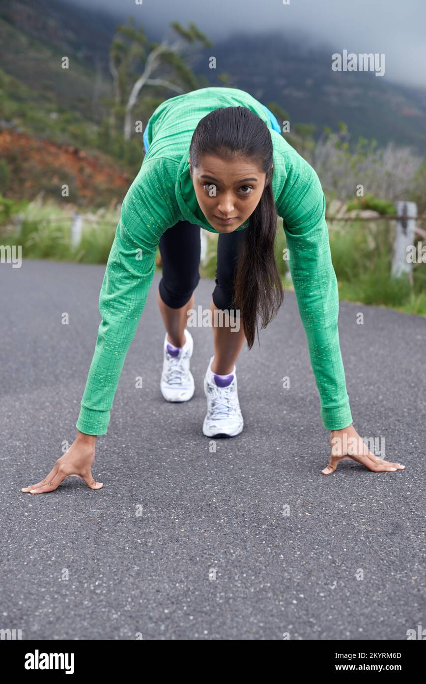 Bereit, diese Straße zu ihrer eigenen zu machen... Eine junge Frau, die auf der Straße hockend, um zu laufen. Stockfoto