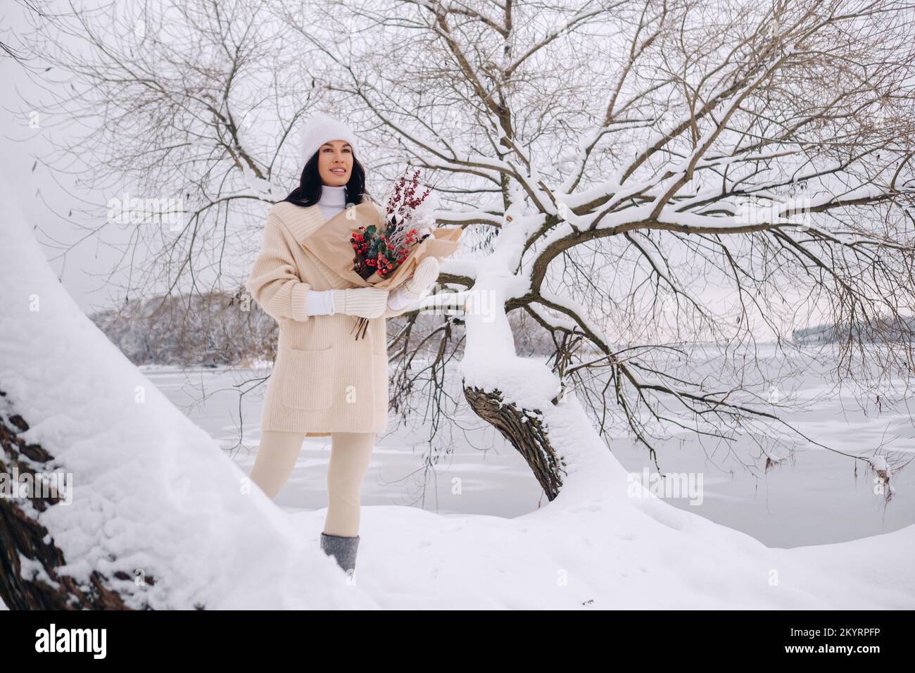 Ein Mädchen in einer beigen Strickjacke und Winterblumen geht in der Schneesaison in der Natur spazieren. Winterwetter Stockfoto