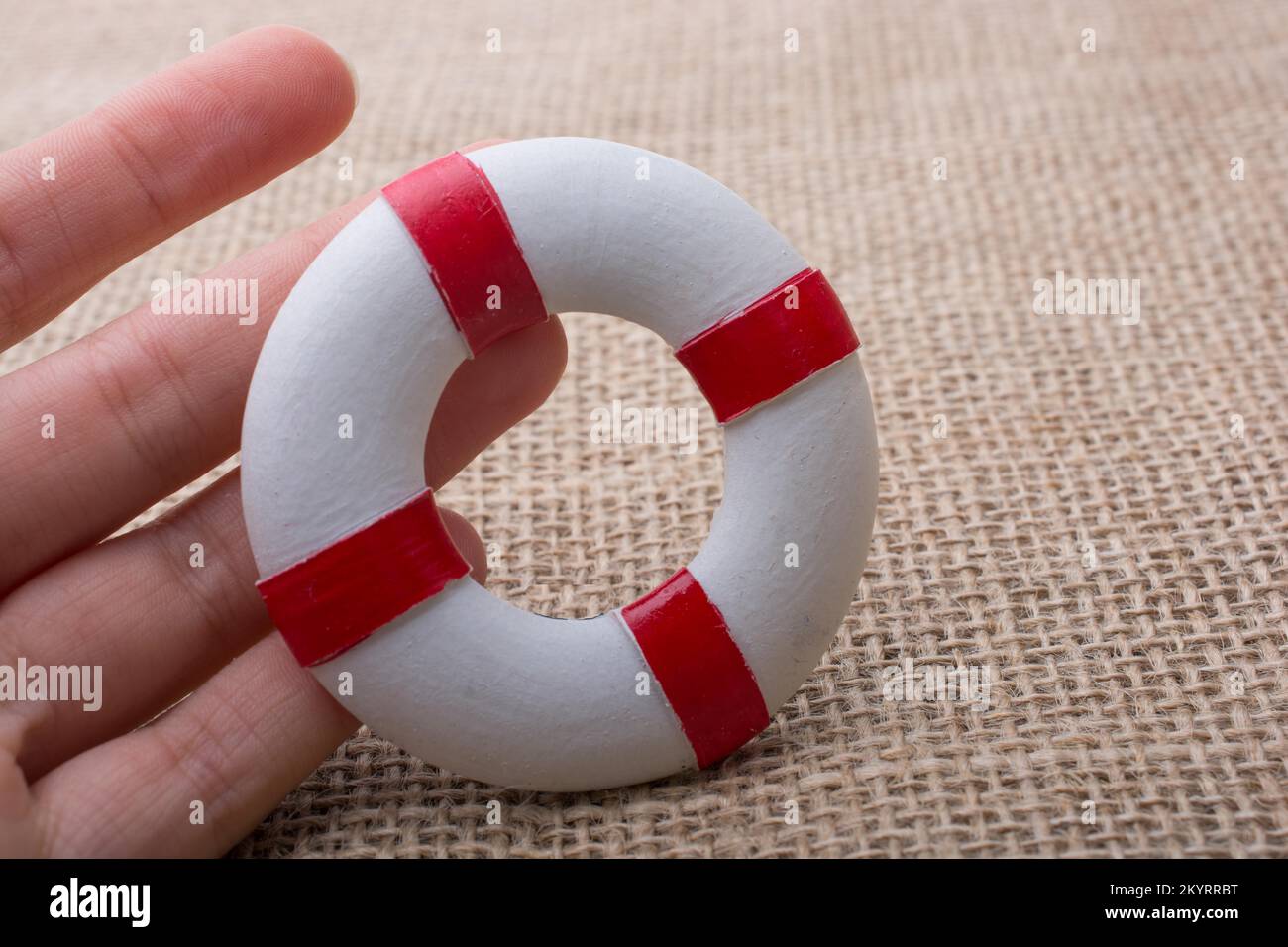 Hand, die einen Lifesaver oder eine Rettungsweste auf einem Stoffhintergrund hält Stockfoto Hand, die einen Lifesaver oder eine Rettungsweste auf einem Stoffhintergrund hält Stockfoto