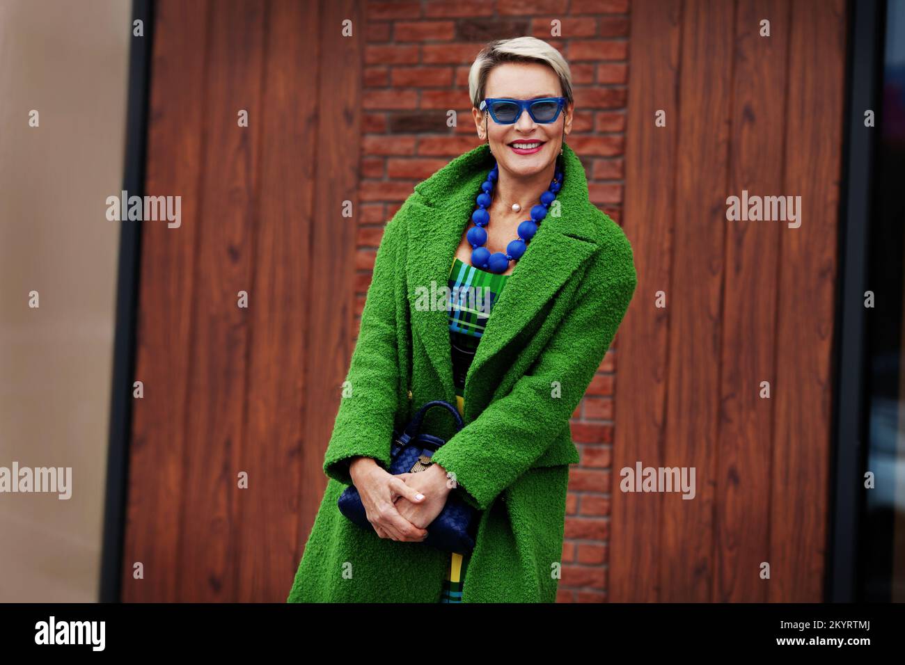 Porträt einer lächelnden stilvollen Frau mit grünem Mantel und blauen Accessoires. Farbenfrohes, trendiges Outfit. Glückliches 45-50-jähriges Modell mit kurzer Fash Stockfoto
