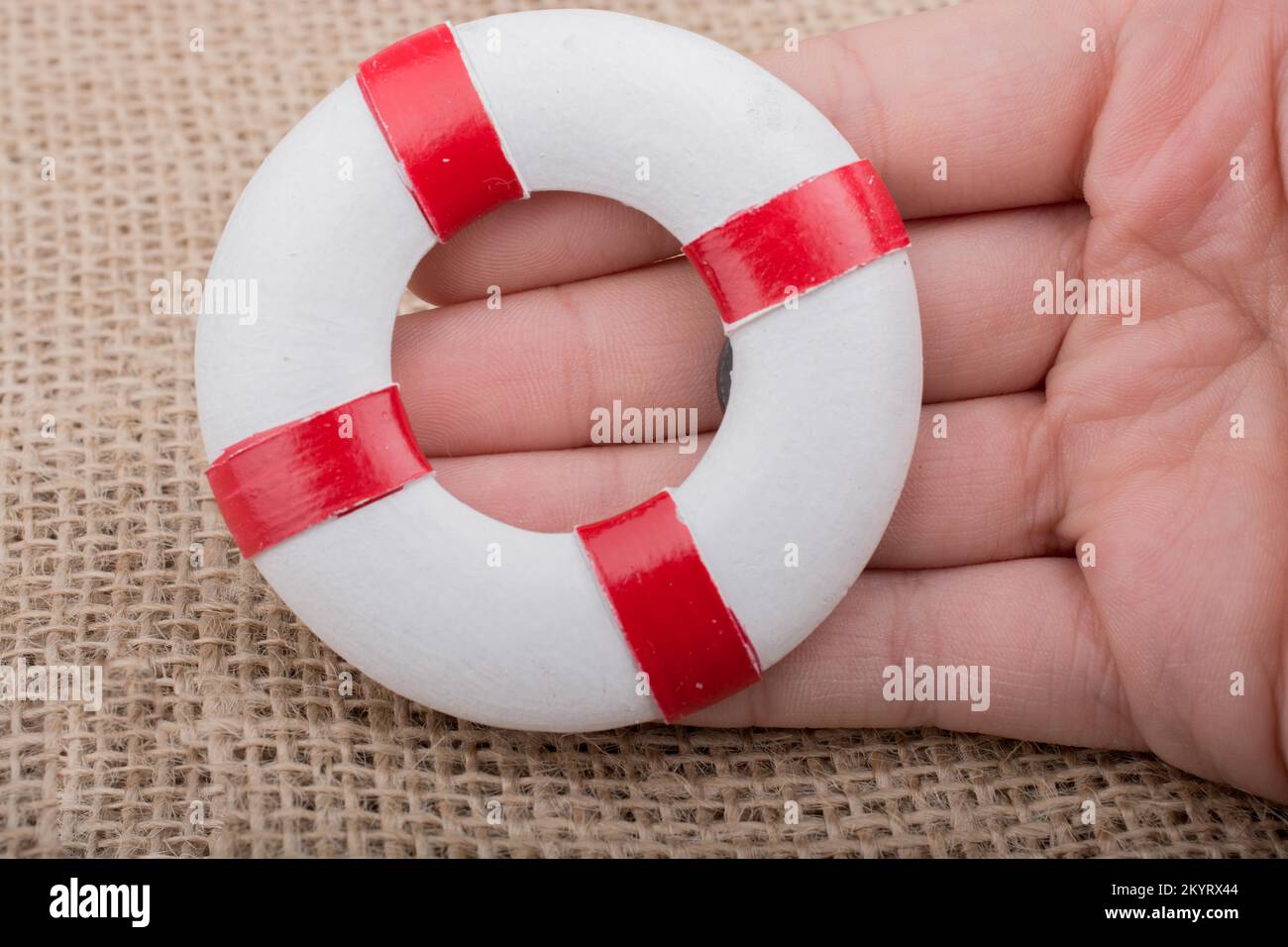 Hand, die einen Lifesaver oder eine Rettungsweste auf einem Stoffhintergrund hält Stockfoto Hand, die einen Lifesaver oder eine Rettungsweste auf einem Stoffhintergrund hält Stockfoto