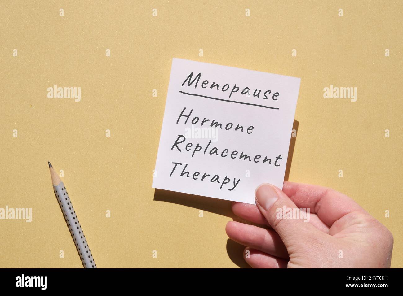 Handgehaltene Papierseite mit Text Menopause, Hormonersatztherapie. Draufsicht auf gelbem einfarbigem Papierhintergrund mit Bleistift. Schreiben auf Blankoschreibung Stockfoto