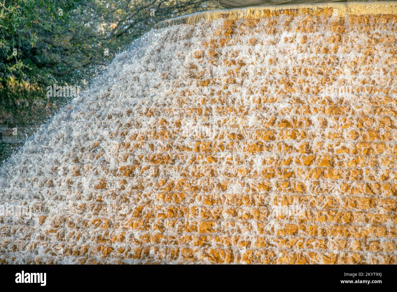 Springbrunnen mit sprudelndem Wasser, das die gelbe Steinmauerwand hinunterläuft. Malerische Ausblicke im Freien in San Antonio Texas mit einer wunderschönen und alten Dekoration Stockfoto