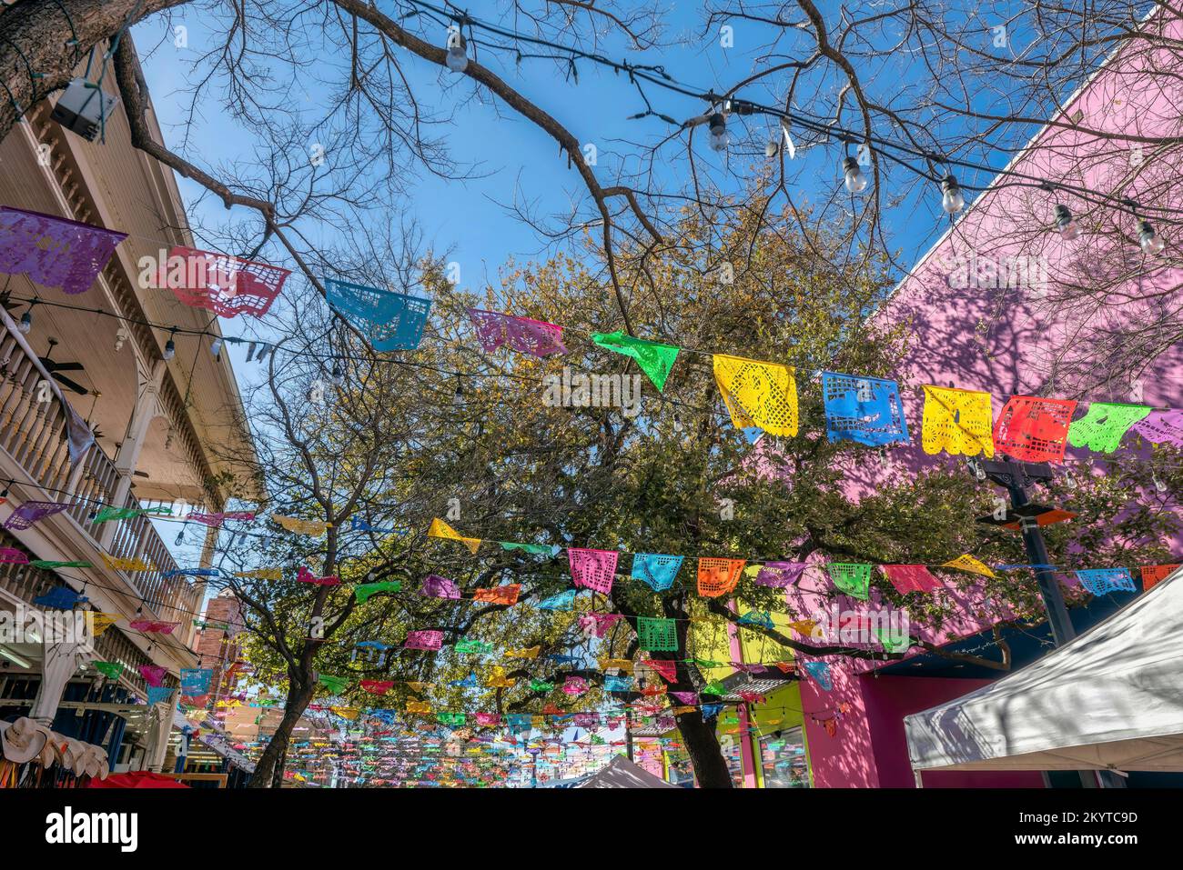 San Antonio, Texas – Fiesta-Flaggen und Lichterketten am River Walk. Farbenfrohe Flaggen an den Bäumen und farbenfrohe Gebäude an den Seiten. Stockfoto