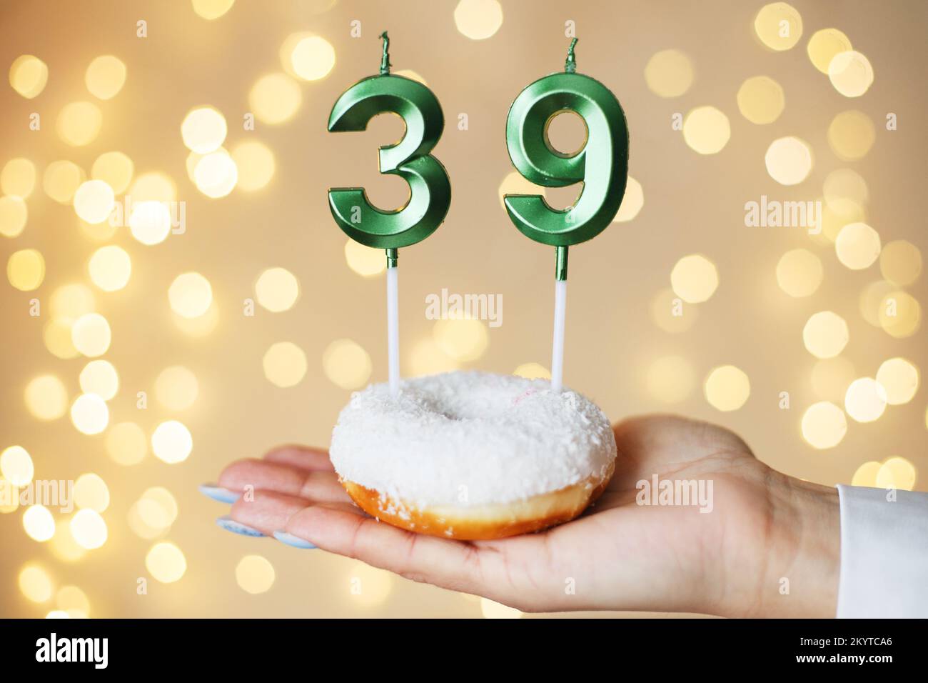 Eine Frau, die einen Kuchen mit den Kerzen Nummer 39 auf festlichem, verschwommenem Bokeh-Hintergrund hält. Stockfoto