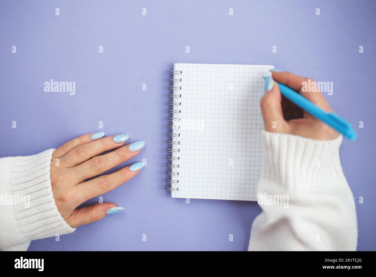 Frauenhand mit Winternägeln hält Stift auf Notizbuch und schreibt Wunschzettel. Stockfoto