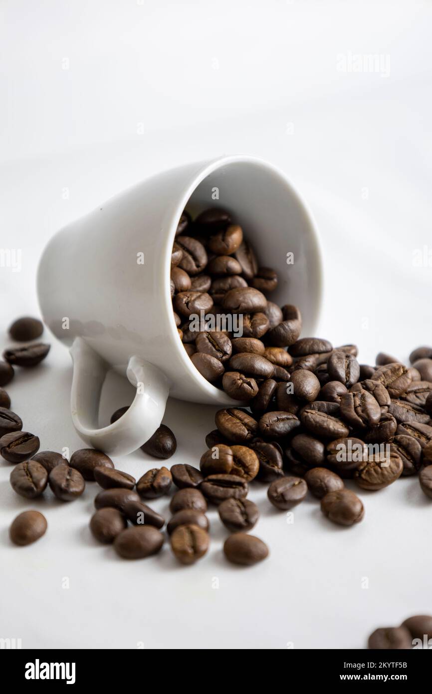 Verschüttete Kaffeebohnen aus einer Tasse. Weißer Hintergrund. Stockfoto
