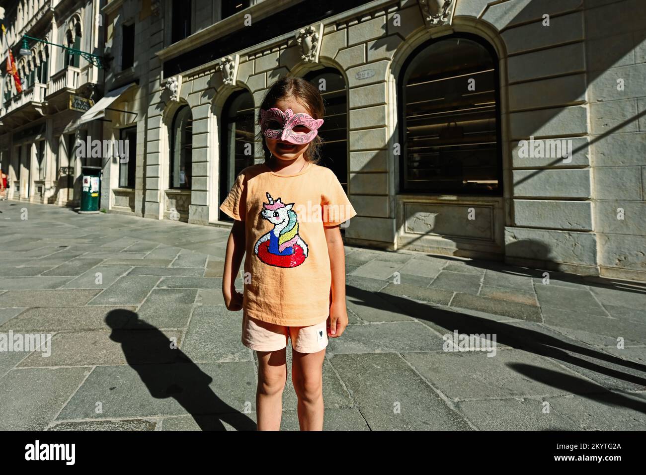 Ein kleines Mädchen trägt eine venezianische Maske in der Straße von Venedig, Italien. Stockfoto