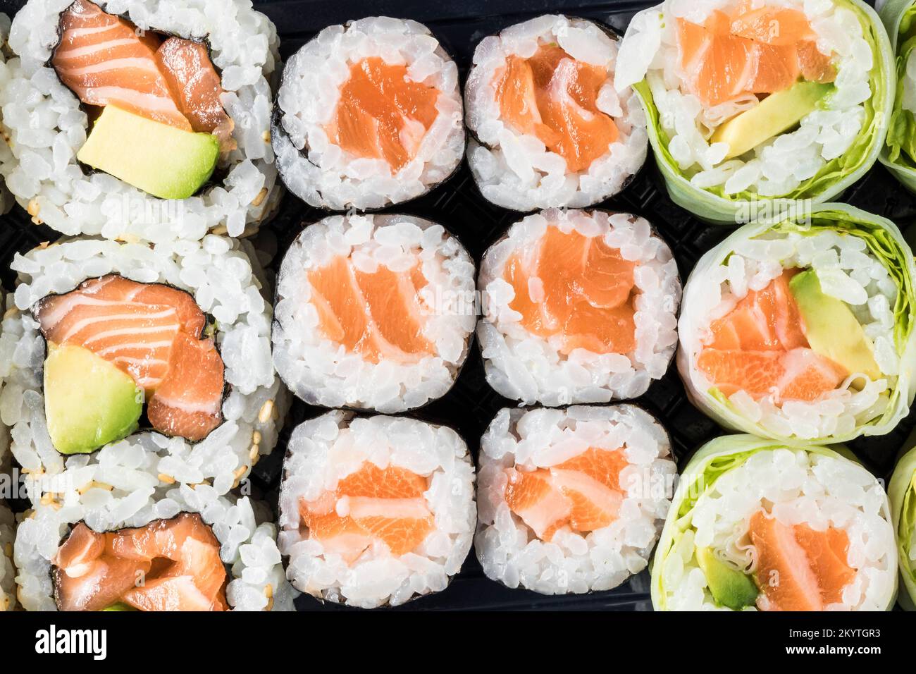 Blick von oben auf ein Tablett mit Lachs Makis verschiedener Arten zum Mitnehmen. Orientalisches, japanisches Essen. Essen. Aufnahme mit Makroobjektiv. Stockfoto