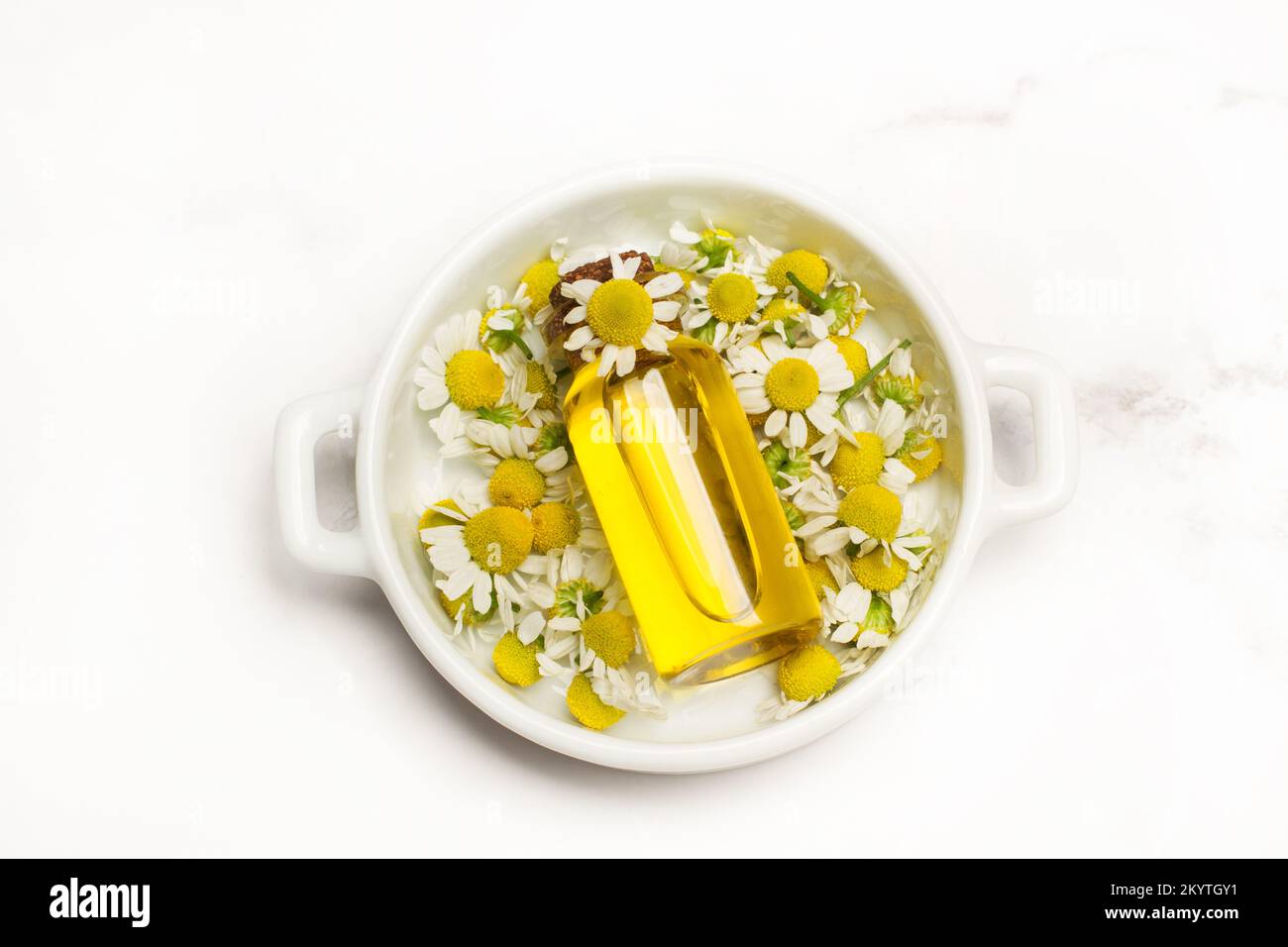 Daisy-Blumen und eine Flasche Olivenöl auf einem weißen Teller auf einer Marmorküche mit Blick von oben Stockfoto