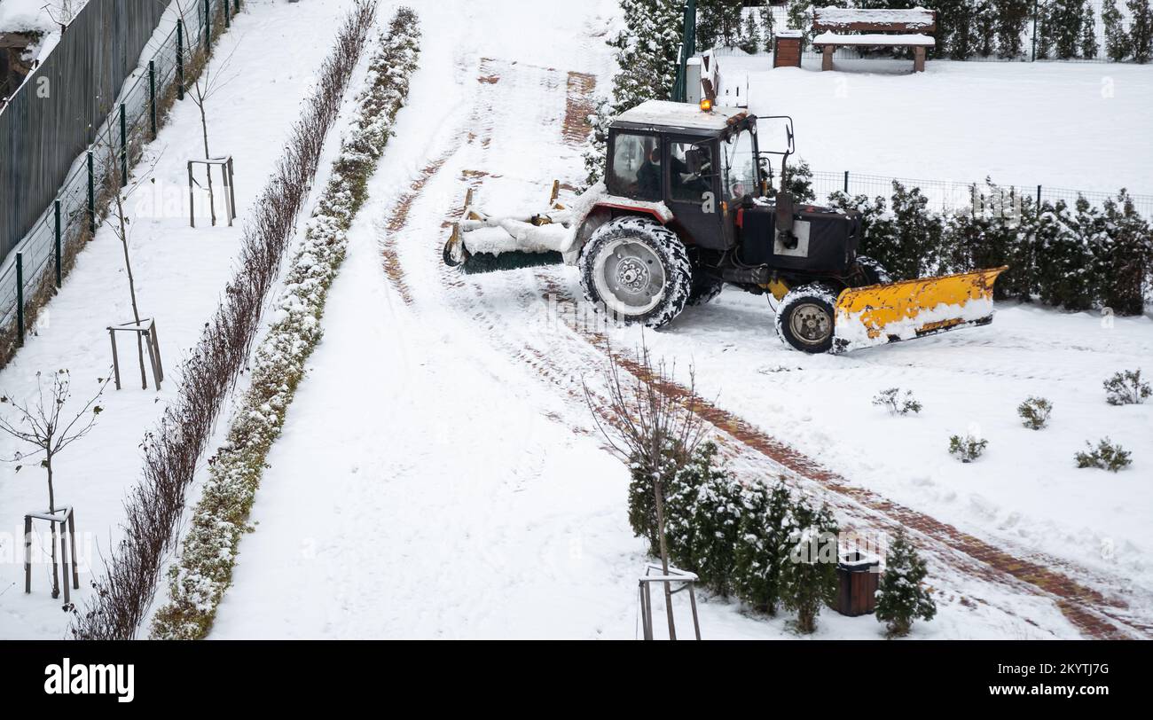 Traktor fegen Schnee mit rotierendem Pinsel und Schneepflug aus der Fußgängerzone auf der Brücke, Schneemanagement auf dem Bürgersteig bei Schneestürmen. Schneepflug entfernen Stockfoto