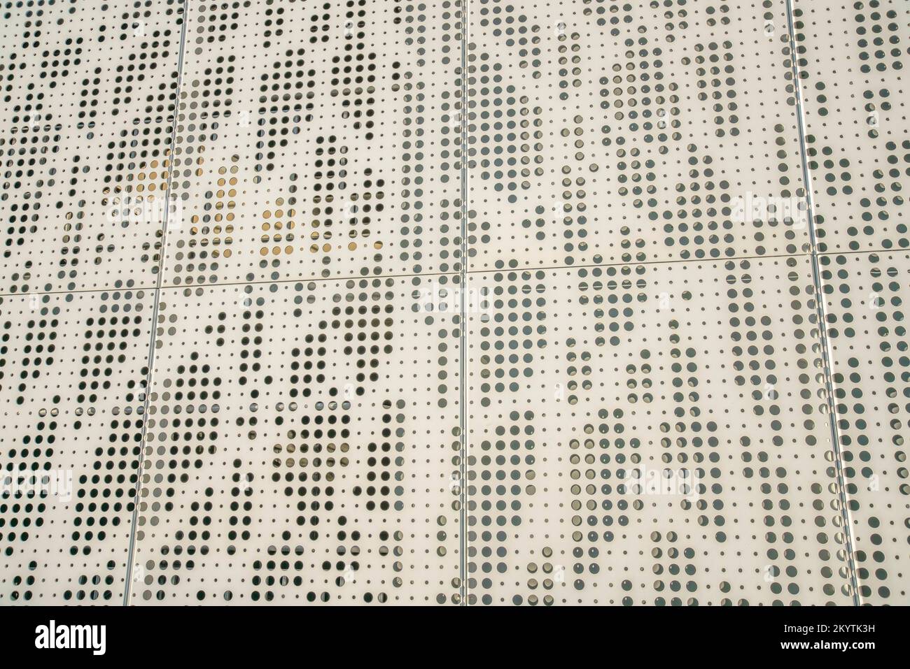 Beige Blechwand mit Löchern in Nahaufnahme. Fassade der Gebäudewand mit Metallblech mit ungleichmäßigen Lochgrößen und beige lackiert. Stockfoto