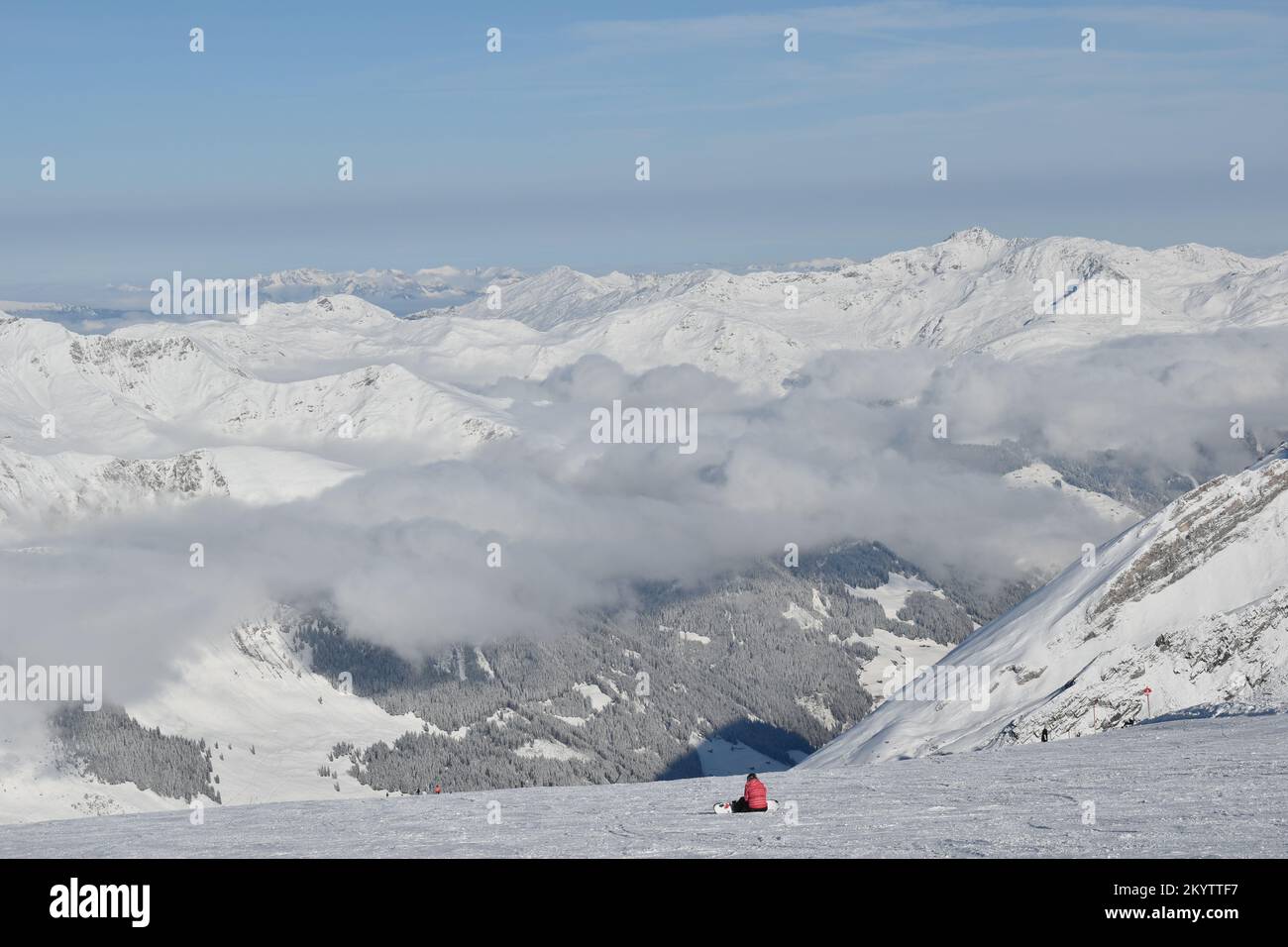 Einsamer Snowboarder, der auf einem Schnee sitzt und im Hintergrund die Winter bedeckten Berge bestaunt Stockfoto