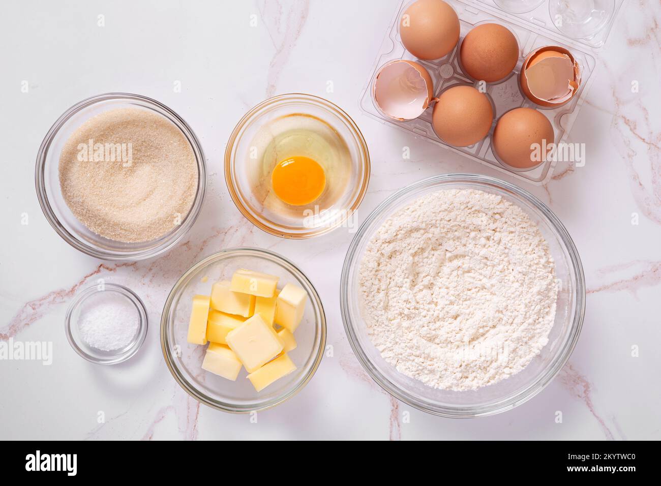 Draufsicht der grundlegenden rohen Backzutaten wie Eier, Zucker, Mehl, Butter, Salz, Auf einer Marmoroberfläche Stockfoto