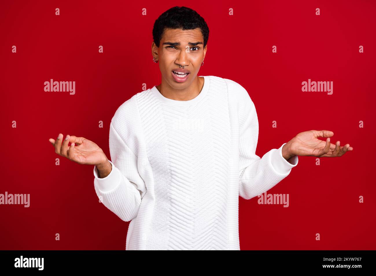Foto eines jungen unzufriedenen Mannes Tragen Sie weißen Pullover Keine Ahnung Schultern zucken wie Probleme mit Weihnachtsgeschenken lösen isoliert auf rotem Hintergrund Stockfoto