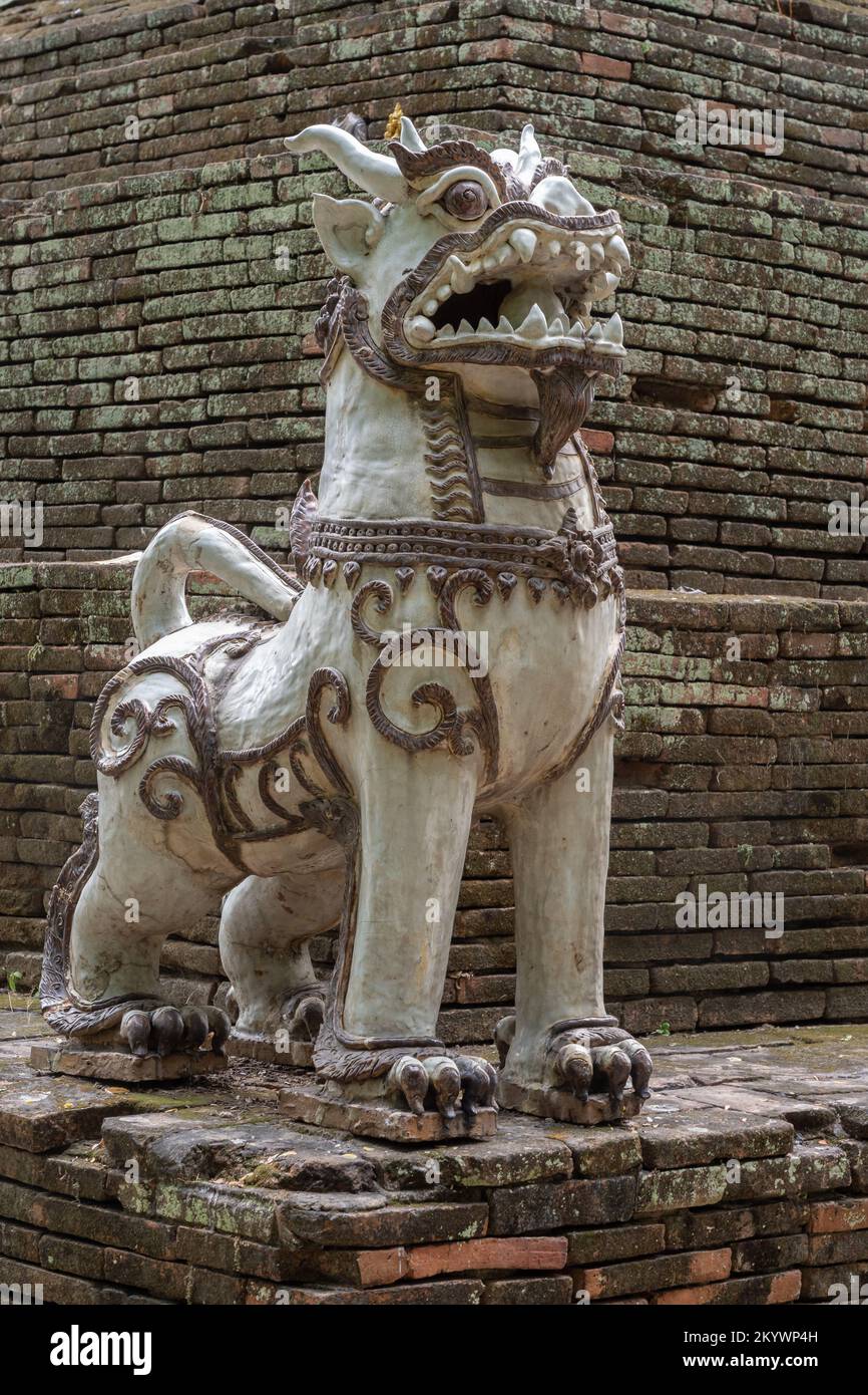 Traditioneller Löwenwächter und Beschützer aus Keramik am Fuße der alten Backsteinstupa des alten Wat Lok Moli oder des buddhistischen Tempels Lok Molee, Chiang Mai, Thailand Stockfoto