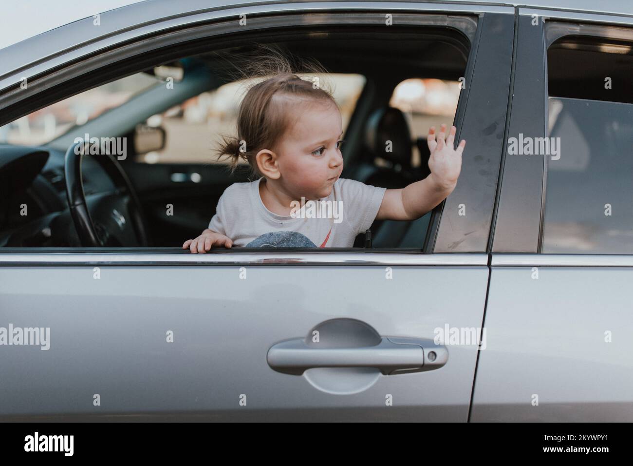 Ein kleines Mädchen, das sich aus dem Autofenster lehnt und Auf Wiedersehen winkt Stockfoto