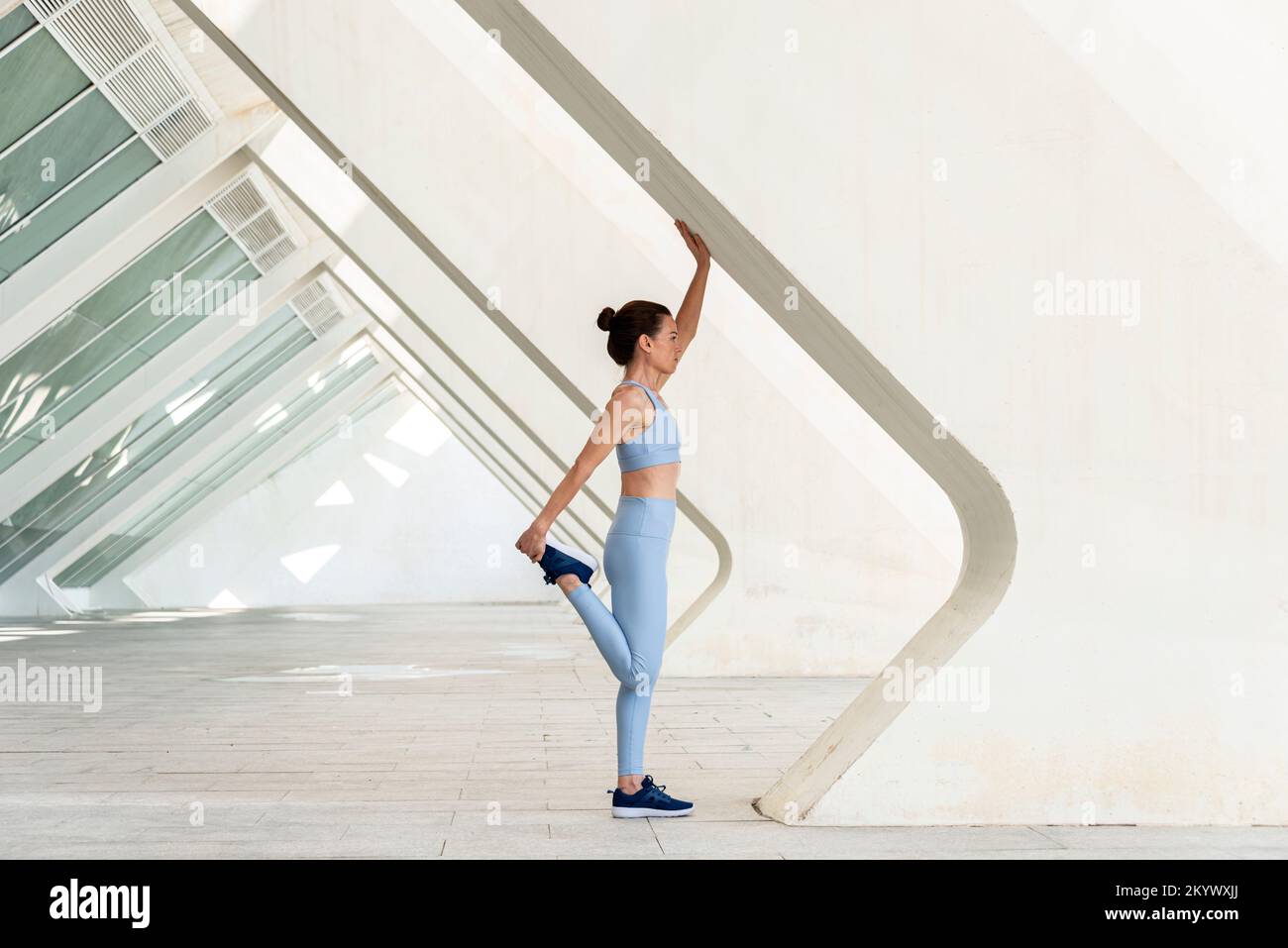 Sportliche Frau mit Beindehnung, Aufwärmübungen. Moderner urbaner Hintergrund. Stockfoto