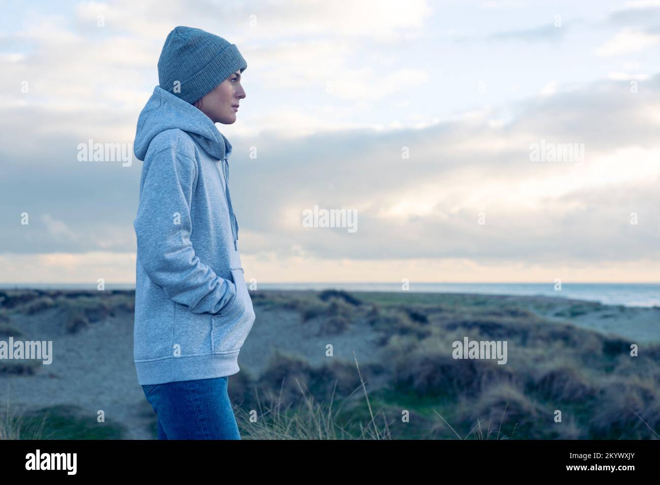 Eine Frau geht alleine am Meer spazieren. Wollmütze und warmer Hoodie. Stockfoto