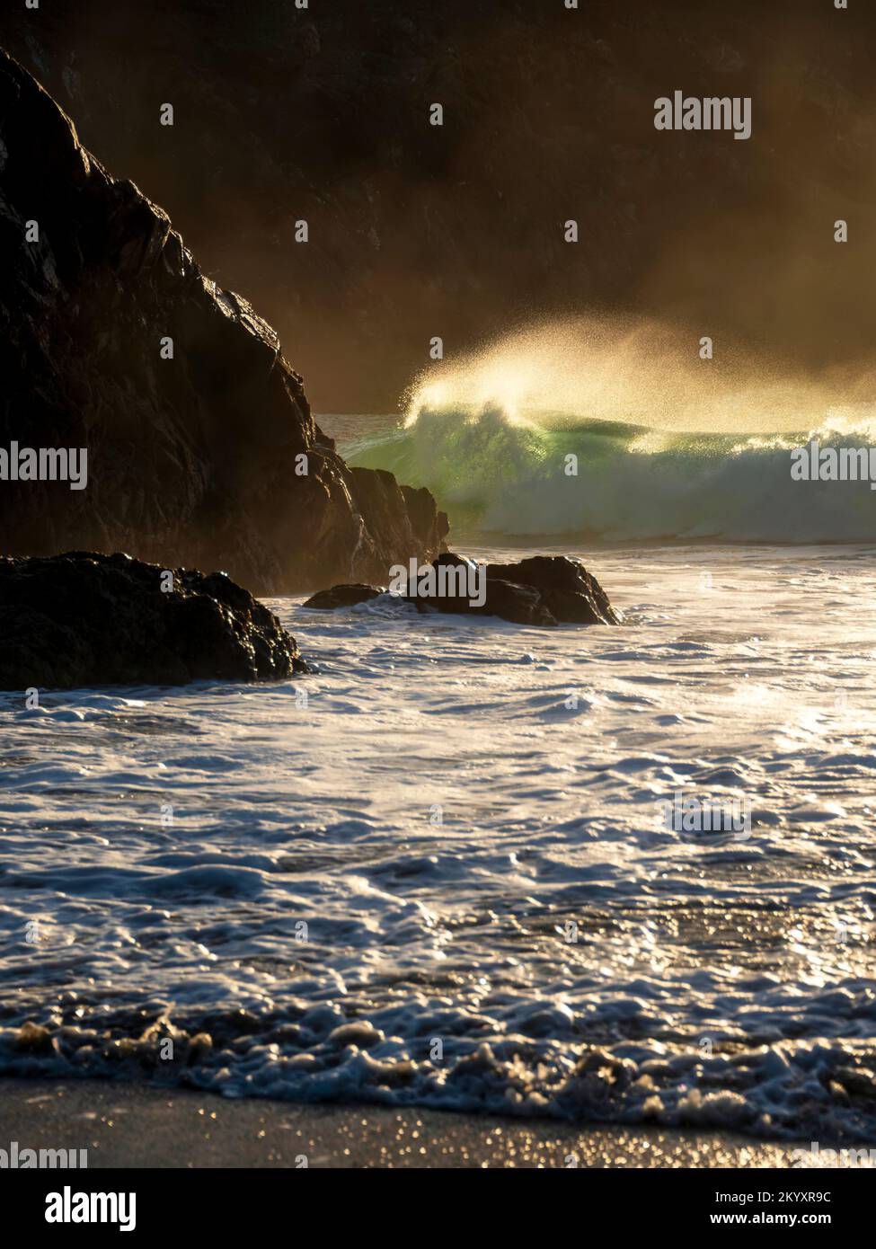 Episches Landschaftsbild von Jade türkisfarbenen Wellen, die in Kynance Cove Cornwall auf Ufer und Felsen krachen, mit leuchtendem Sonnenaufgangshintergrund und Wasserspray dr Stockfoto