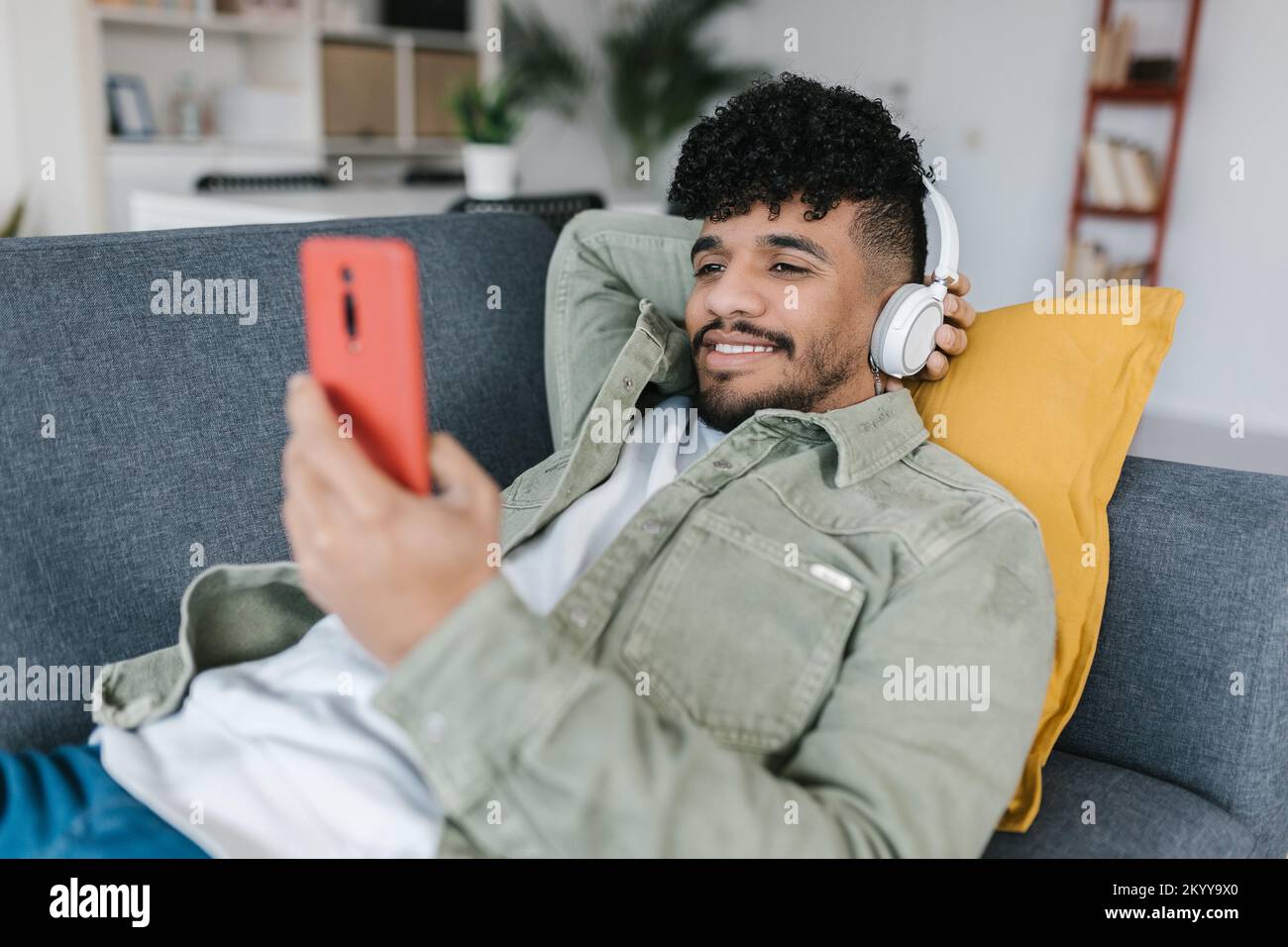 lateinamerikanischer junger Mann, der sich auf dem Sofa entspannt und soziale Medien auf dem Mobiltelefon ansieht Stockfoto