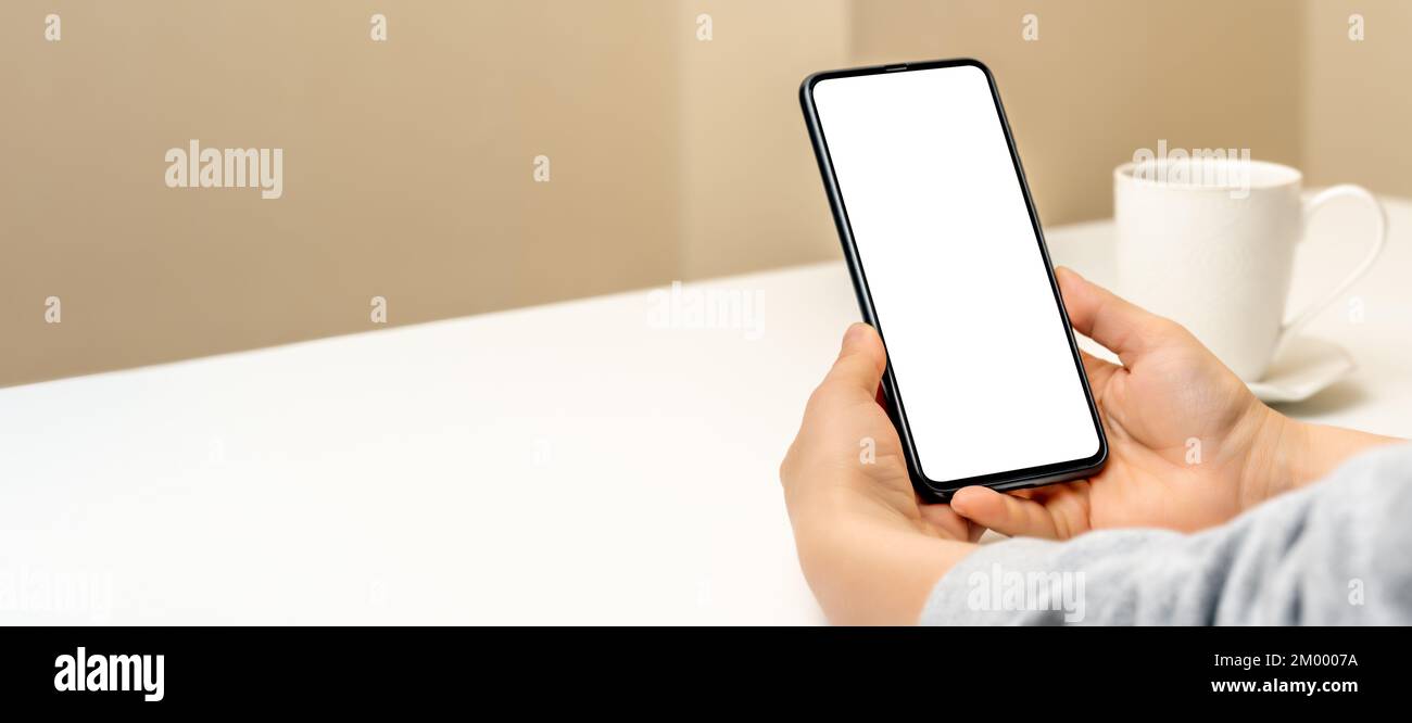 Mockup Handy. Hände der Frau mit Handy vor dem Hintergrund der gelben Wand und Tasse Kaffee. Mockup-Bild der Hände, die das Mobiltelefon mit halten Stockfoto