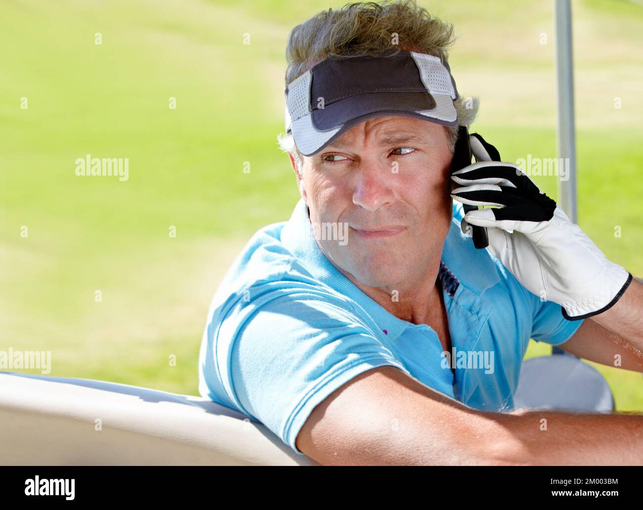 Geschäft und Vergnügen vermischen. Ein reifer Golfer, der in einem Golfwagen sitzt und mit seinem Handy spricht. Stockfoto