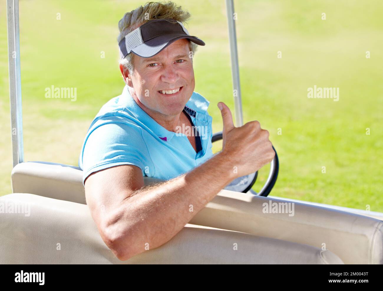 Das ist ein toller Golfplatz. Ein reifer Golfer, der Ihnen die Daumen nach oben zeigt, wenn er in seinem Golfwagen sitzt. Stockfoto