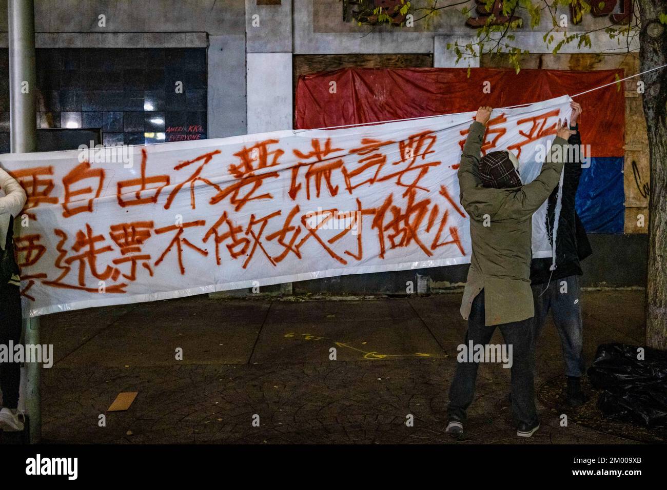 Boston, Usa. 02.. Dezember 2022. Demonstranten hängen ein Banner auf, auf dem steht: "Wir wollen Nahrung, keine covid-Tests; wir wollen Reformen, nicht kulturelle Revolution", vor einer Kerzenschein-Mahnwache im Tiananmen Memorial. Mehr als 400 Menschen nehmen an einer Nachtwache bei Kerzenschein am Tiananmen Memorial in Boston Chinatown Teil, um gegen Chinas Null-Covid-Politik zu protestieren und den Opfern des tragischen Feuers von Urumqi am 2. Dezember 2022 zu gedenken. (Foto: Tang Ka Huen/SOPA Images/Sipa USA) Guthaben: SIPA USA/Alamy Live News Stockfoto