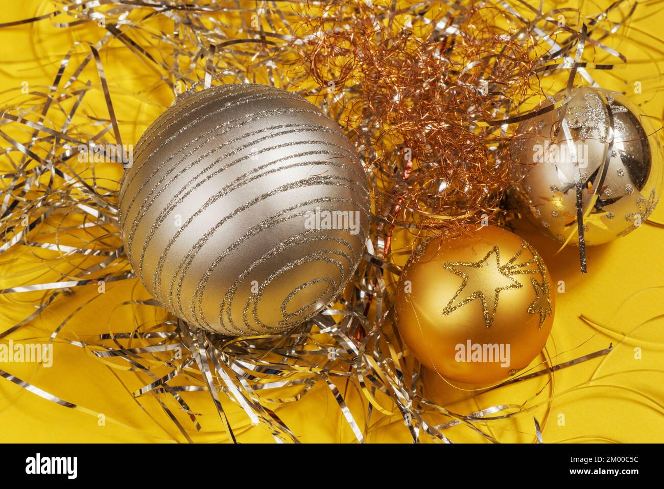 Drei dekorative silberne und goldene weihnachtskugeln auf einem Bündel metallischer Fäden auf gelbem Hintergrund. Stockfoto