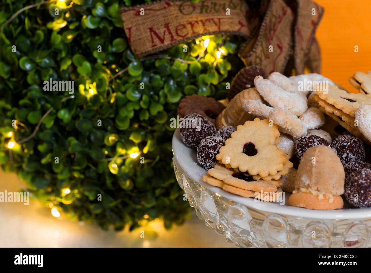 Kleine, glänzende weihnachtsbaumkugel mit Band „Merrry christmas“ und vielen kleinen traditionellen weihnachtskeksen in einer Glasschüssel. Stockfoto