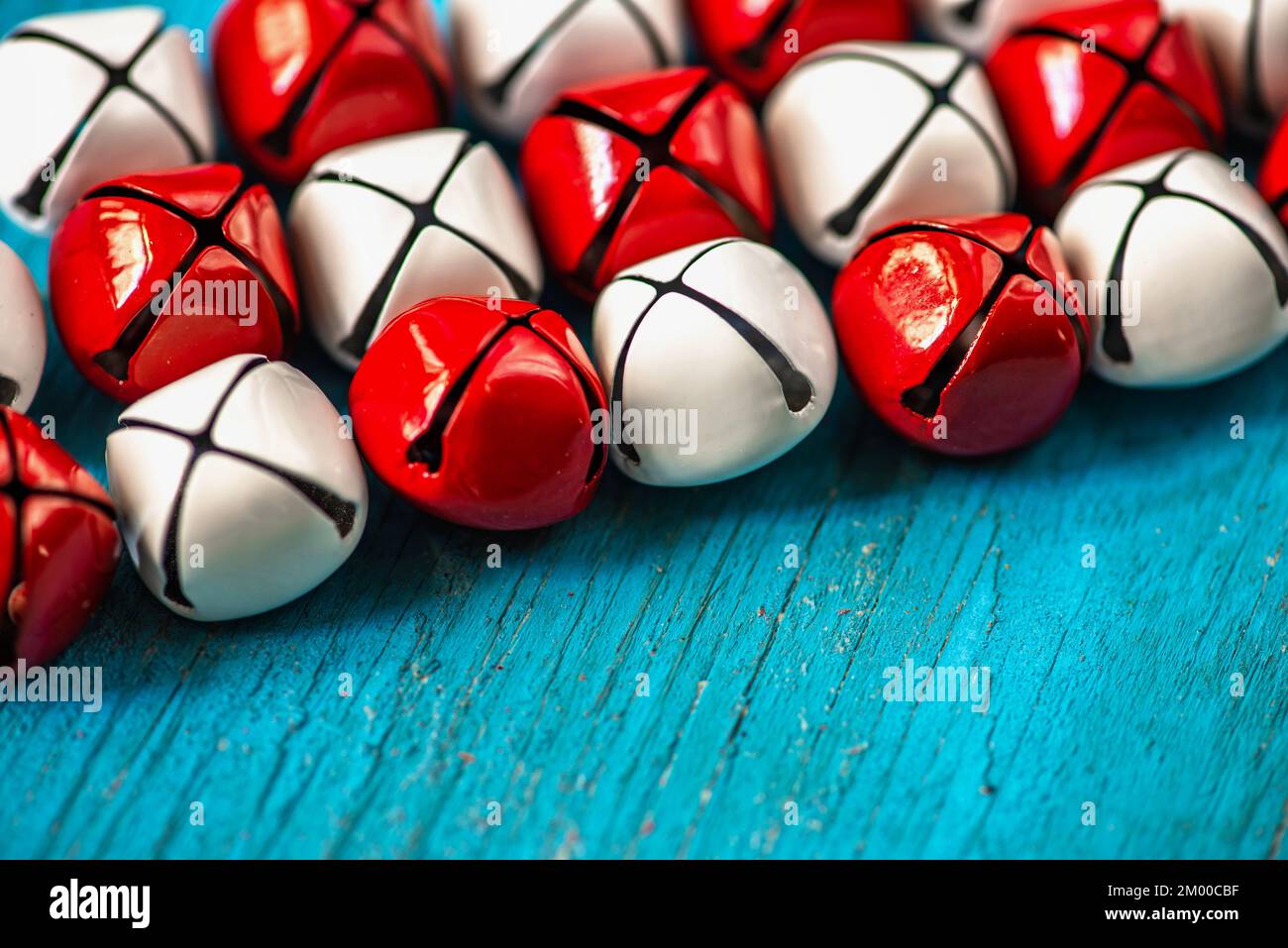 Viele rote und weiße metallische Klingelglocken auf blauem Holzhintergrund, Nahaufnahme. Stockfoto