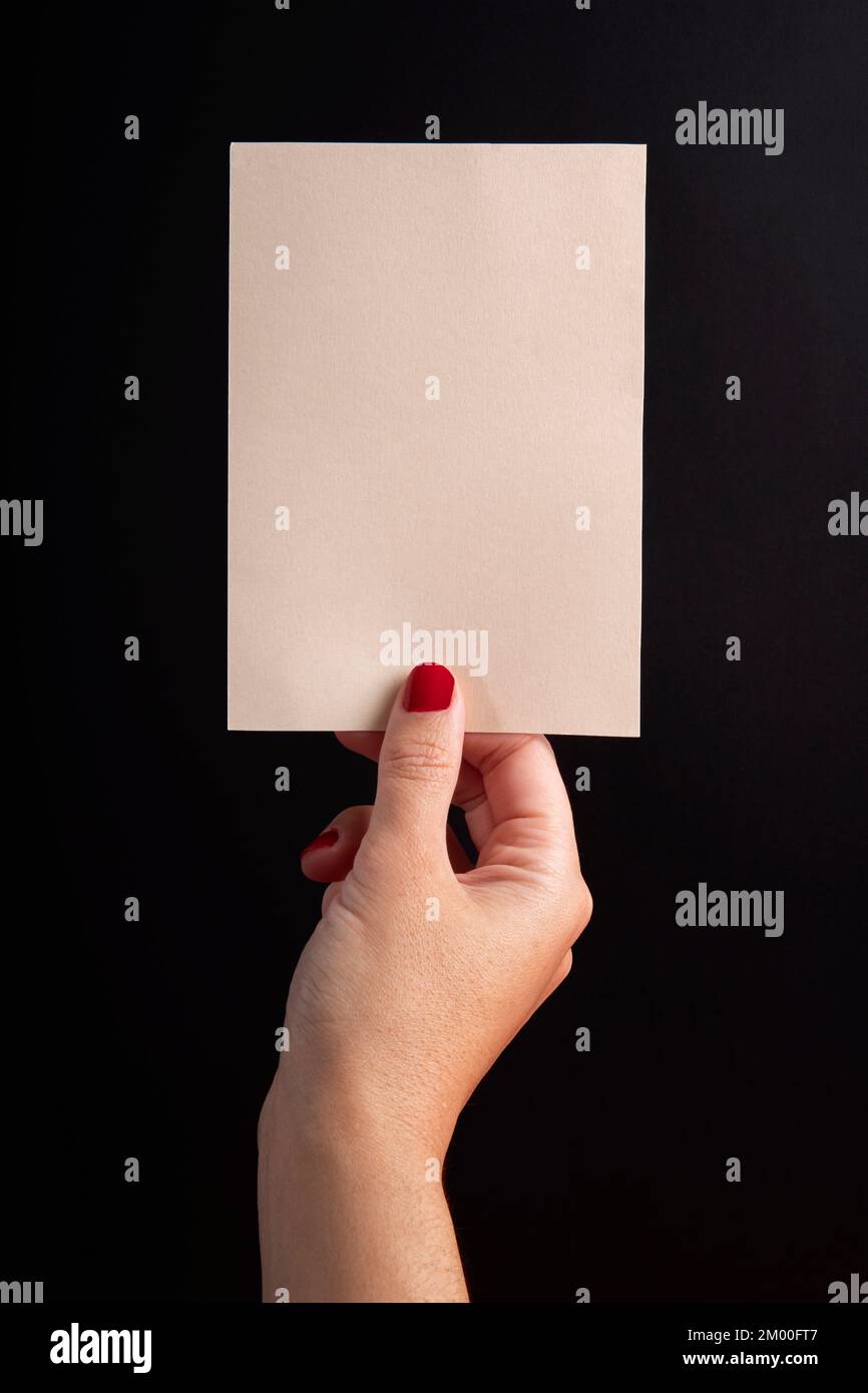 A5-Postkarte im vertikalen Format, gehalten von einer weiblichen Hand auf schwarzem Hintergrund mit Kopierraum und Modell Stockfoto