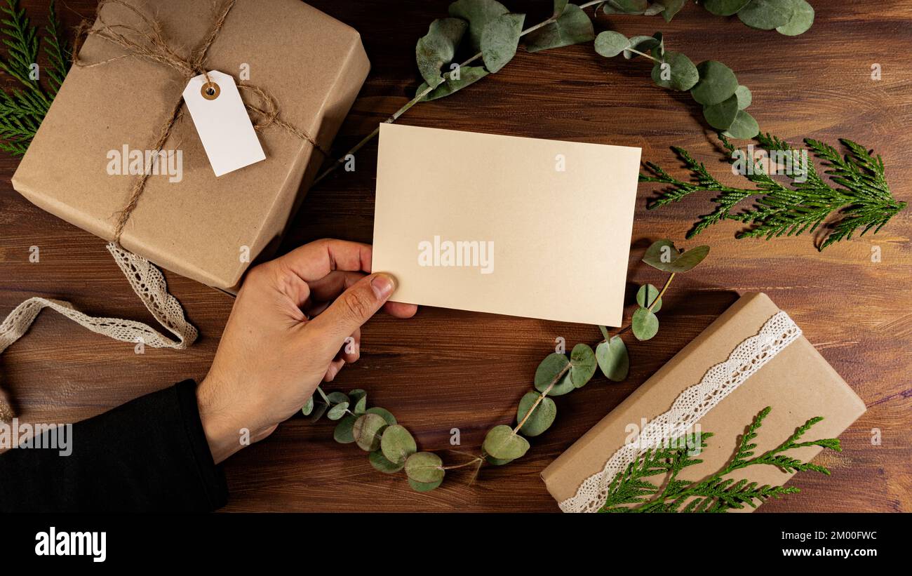 Männerhand, die eine A5 horizontale Postkarte über verpackte Kraftkisten hält Stockfoto