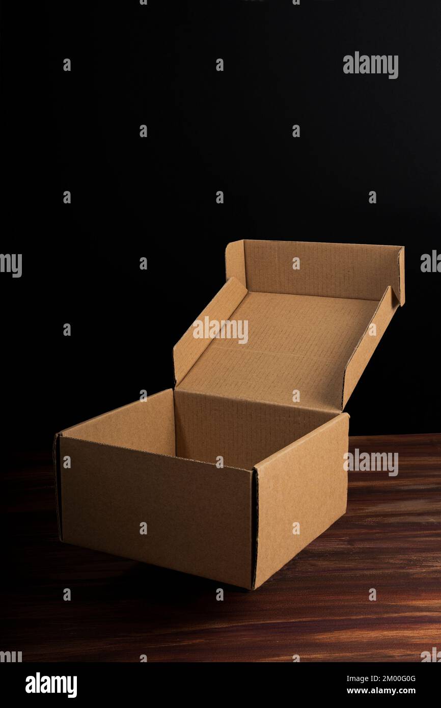 Braune Kartonschachtel, offen über der Holzoberfläche mit schwarzem Hintergrund Stockfoto