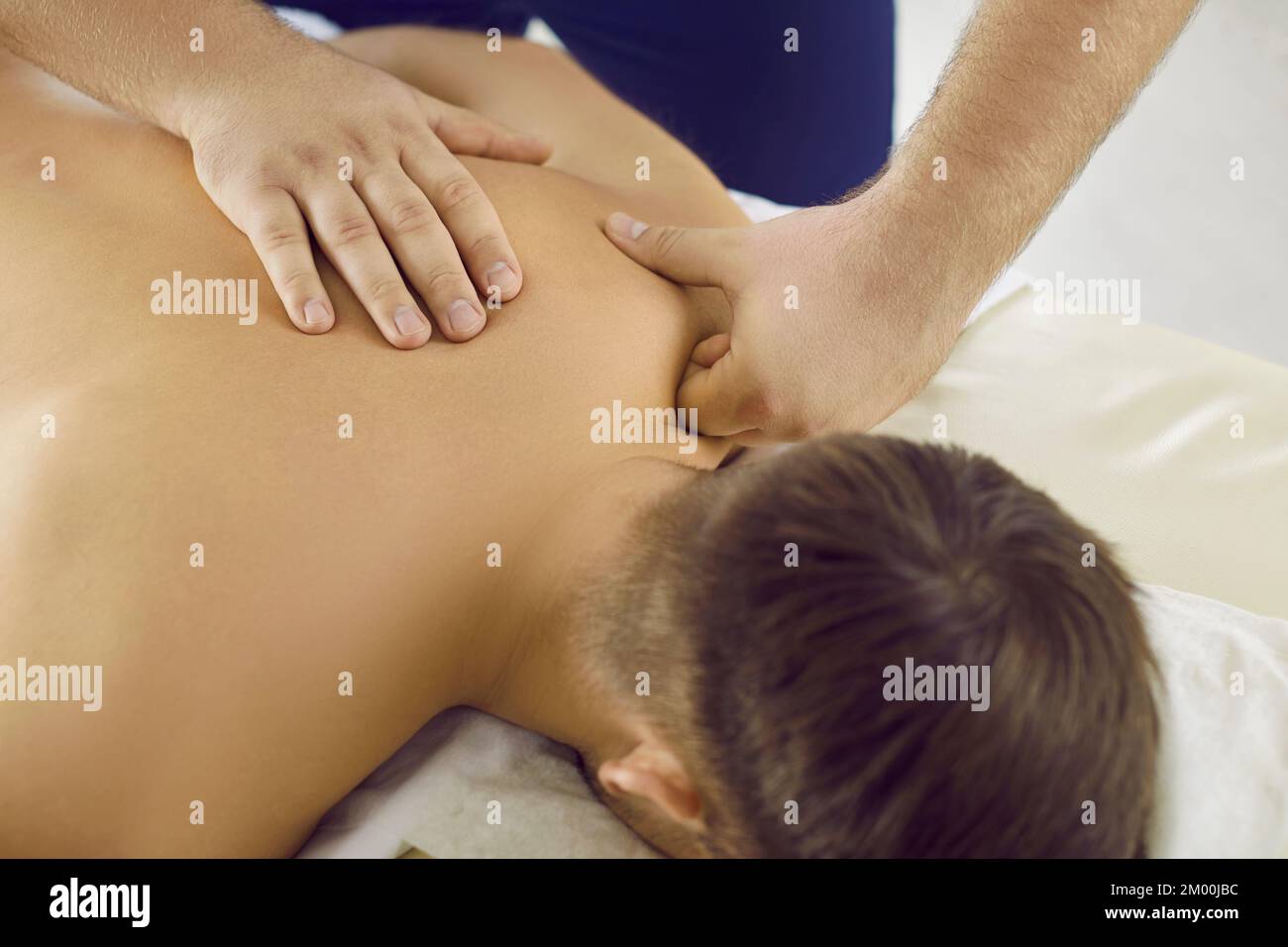 Mann genießt entspannende Rückenmassage, die von einem professionellen Masseur im Massageraum durchgeführt wird Stockfoto