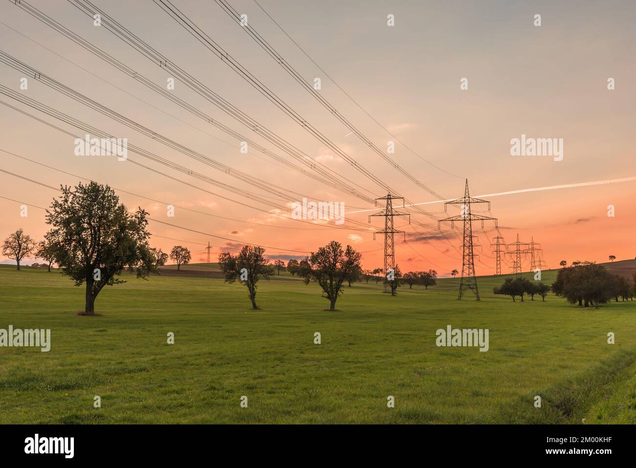 Hochspannungs-Strommasten und Stromleitungen auf einem Feld bei Sonnenuntergang. Stromerzeugung, Umweltfragen und Klimaschutzkonzept Stockfoto