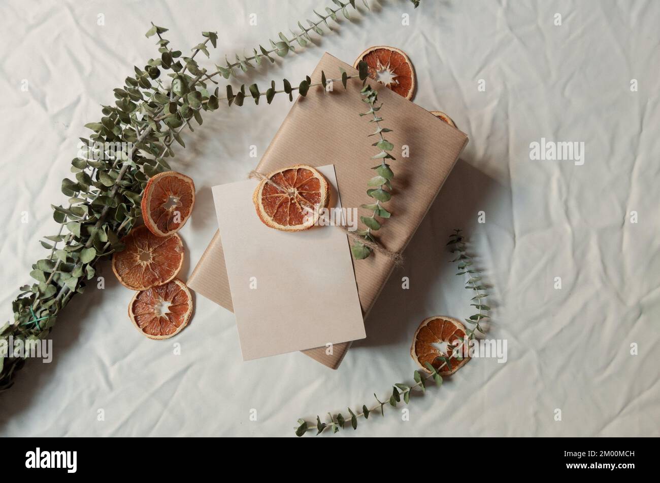 Kleine Businessbox und A5-Postkarte leben noch immer in weißem Hintergrund mit getrockneten orangefarbenen Scheiben und Eukalyptusblättern, umweltfreundliche Verpackung als Geschenk Stockfoto