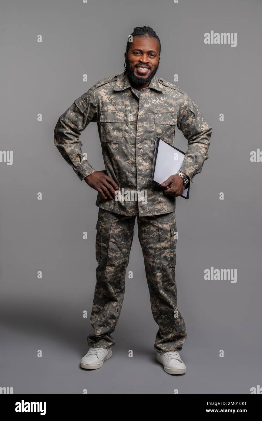 Fröhlicher Soldat, der vor dem grauen Hintergrund für die Kamera posiert. Stockfoto